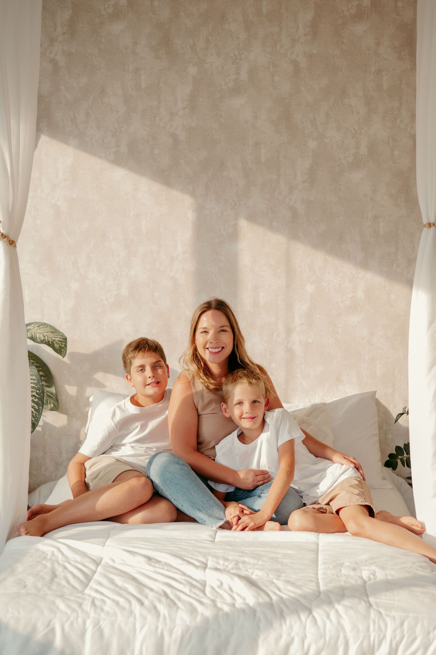 A bright indoor family scene with three people relaxing together on a white bed.