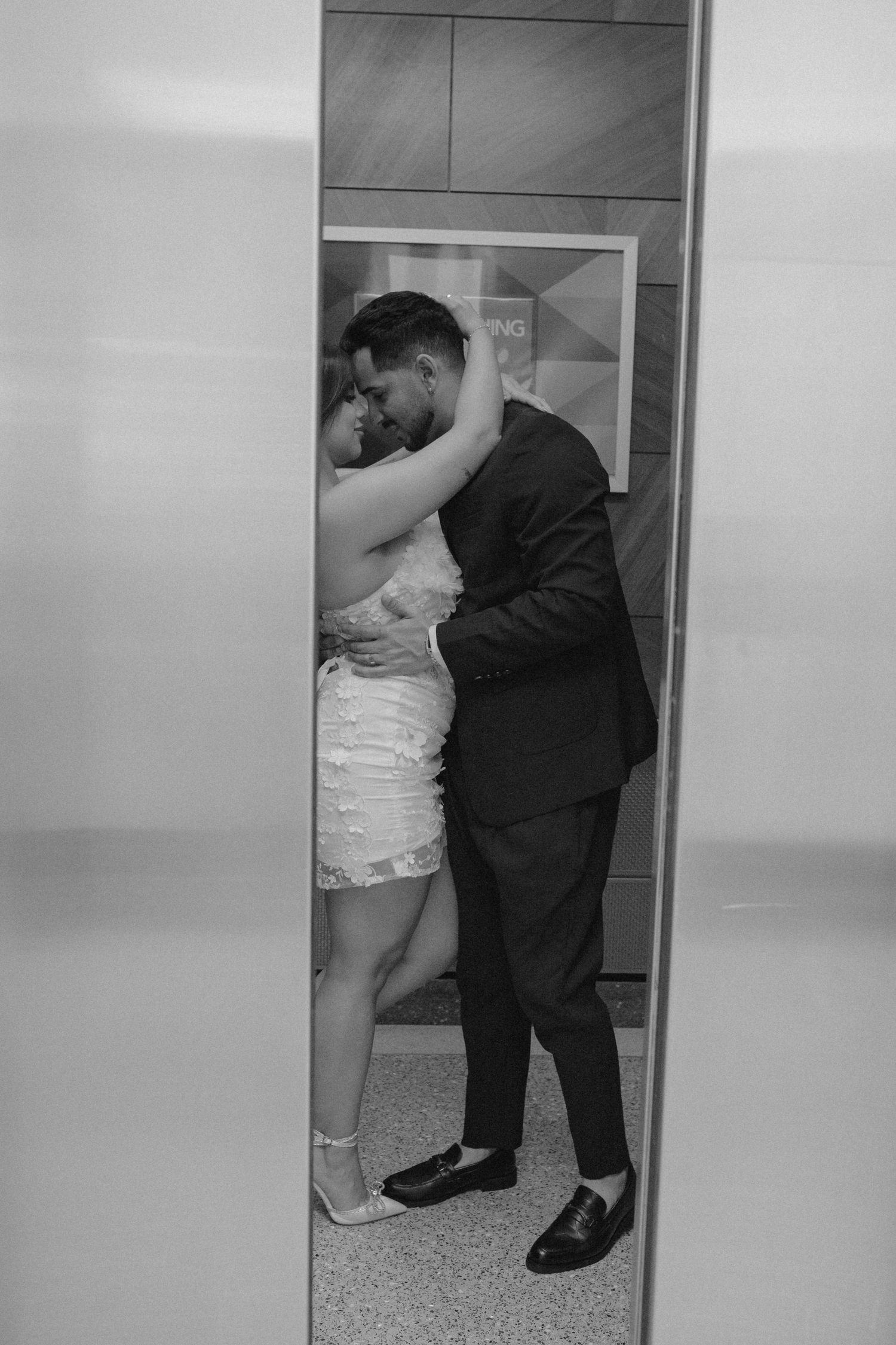 A romantic black and white moment captured in a mirror reflection showing a couple embracing in formal attire.