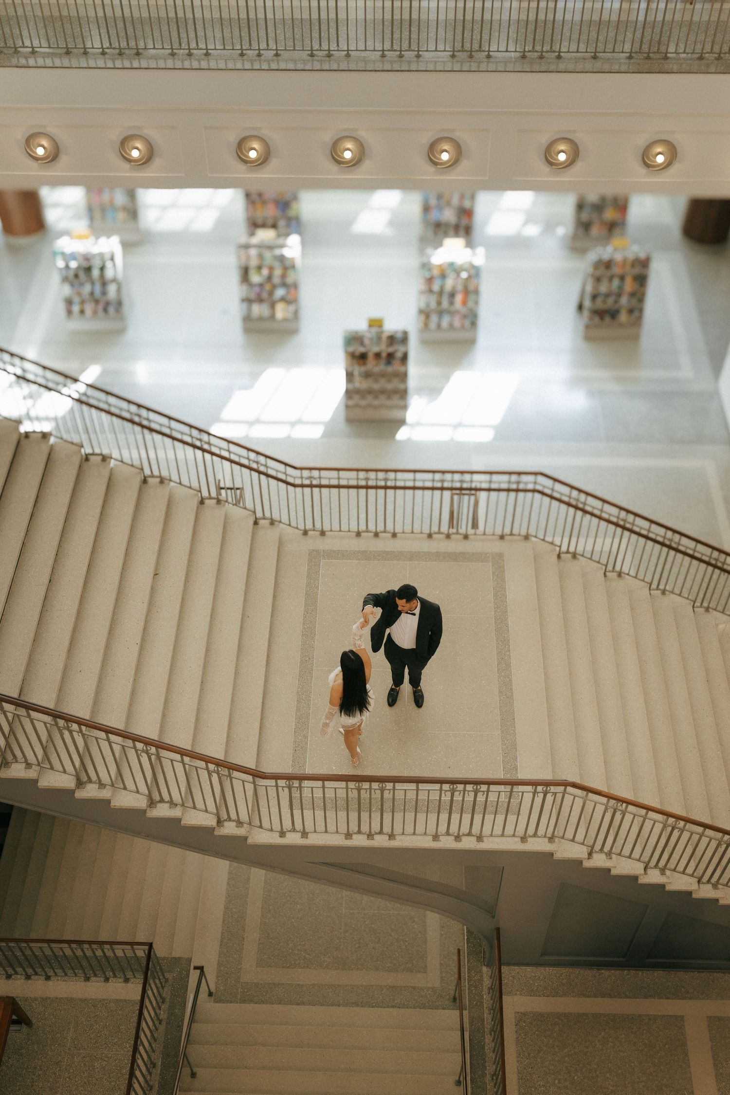 Overhead view of couple standing on elegant white marble staircase in modern building interior.