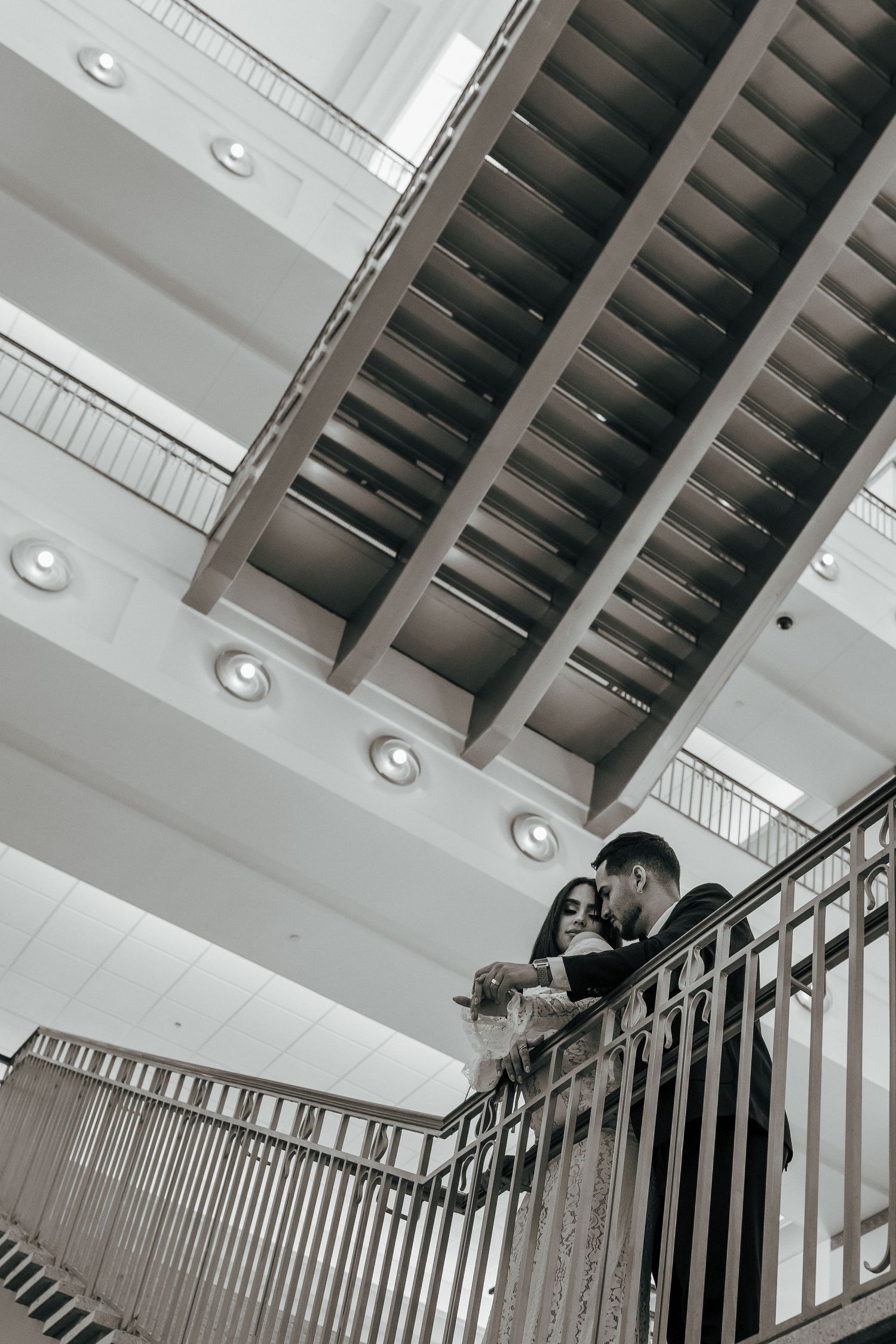 A couple shares an intimate moment on a modern staircase under industrial-style ceiling beams and lighting.