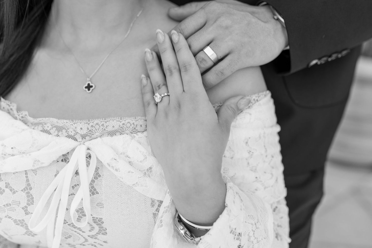Black and white close-up of a bride's hand showing her wedding ring against her lace dress bodice.