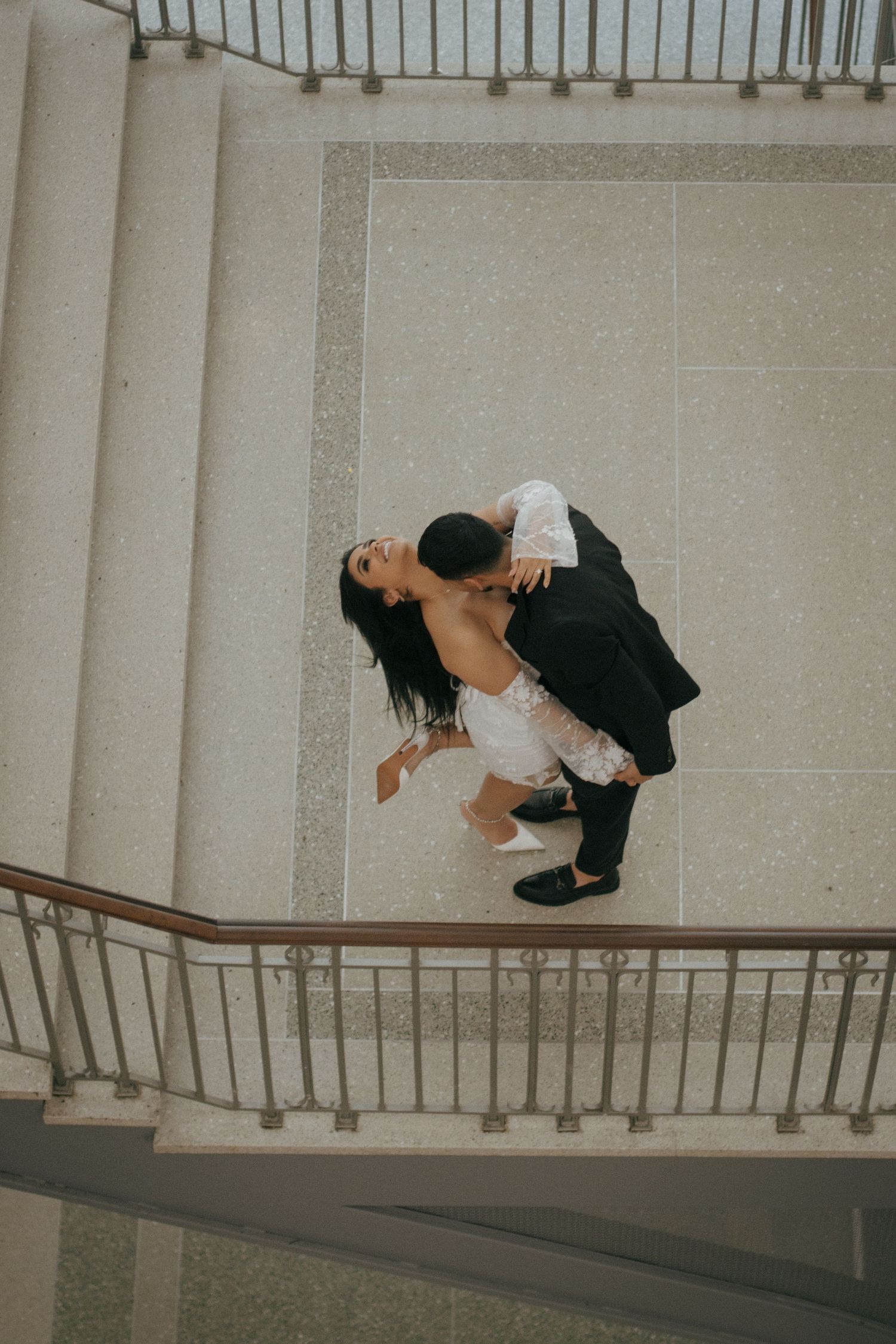Aerial view of a couple dancing on a spiral staircase, the woman dips back gracefully in a white dress.
