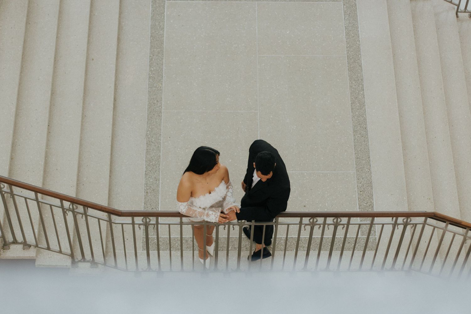 Two people in contrasting white and black attire sit together on an elegant curved staircase railing.