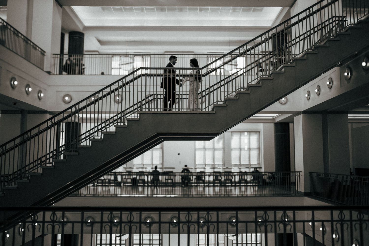 Figure stands on monochromatic staircase in modern architectural interior with geometric lines and multiple levels.