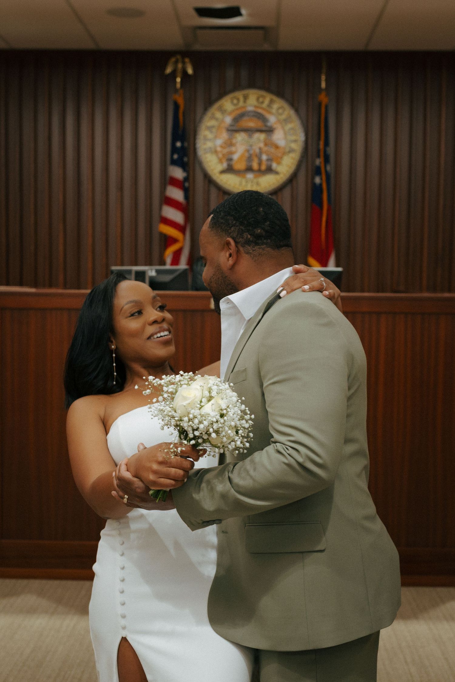 A couple shares a romantic moment during their courthouse wedding ceremony, with state flags and seal visible in background.