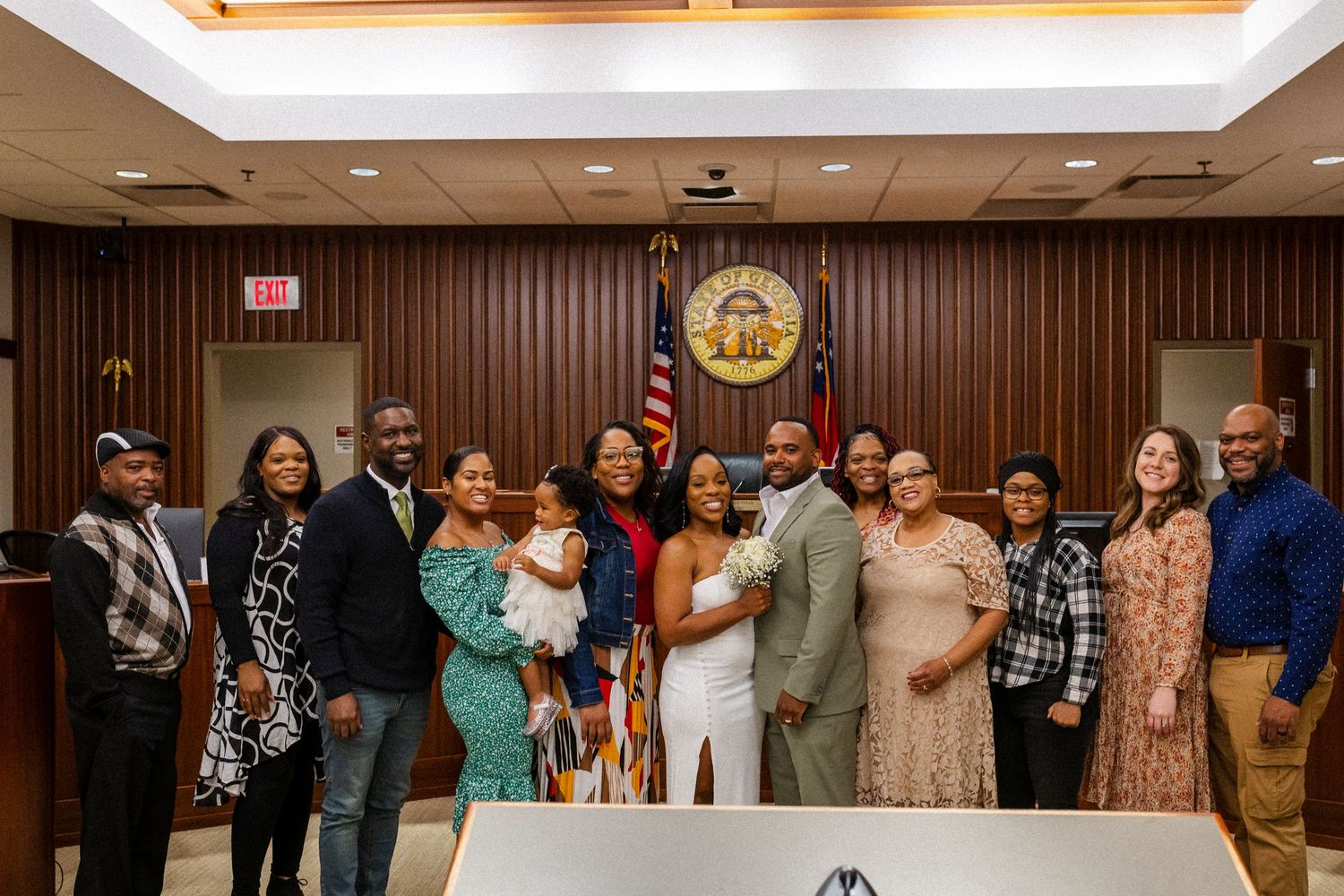 A group photo taken at a formal ceremony in a government building with wood paneling and an official state seal on the wall.
