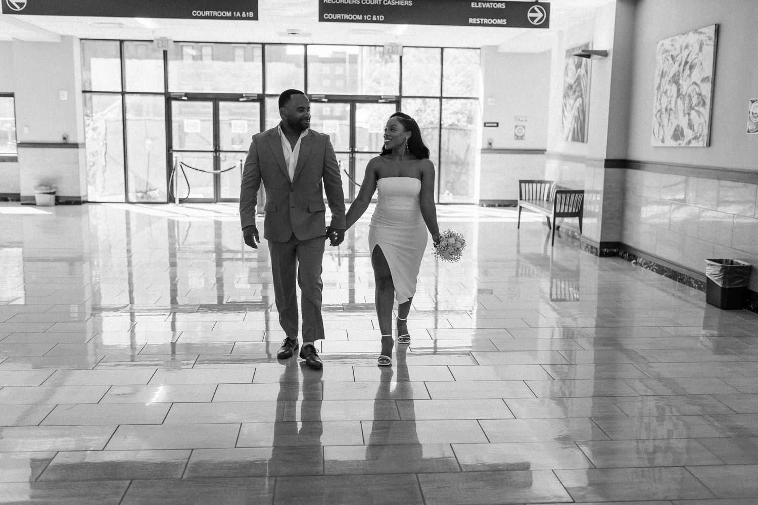 A couple walking hand in hand through a bright modern building interior with reflective floors.