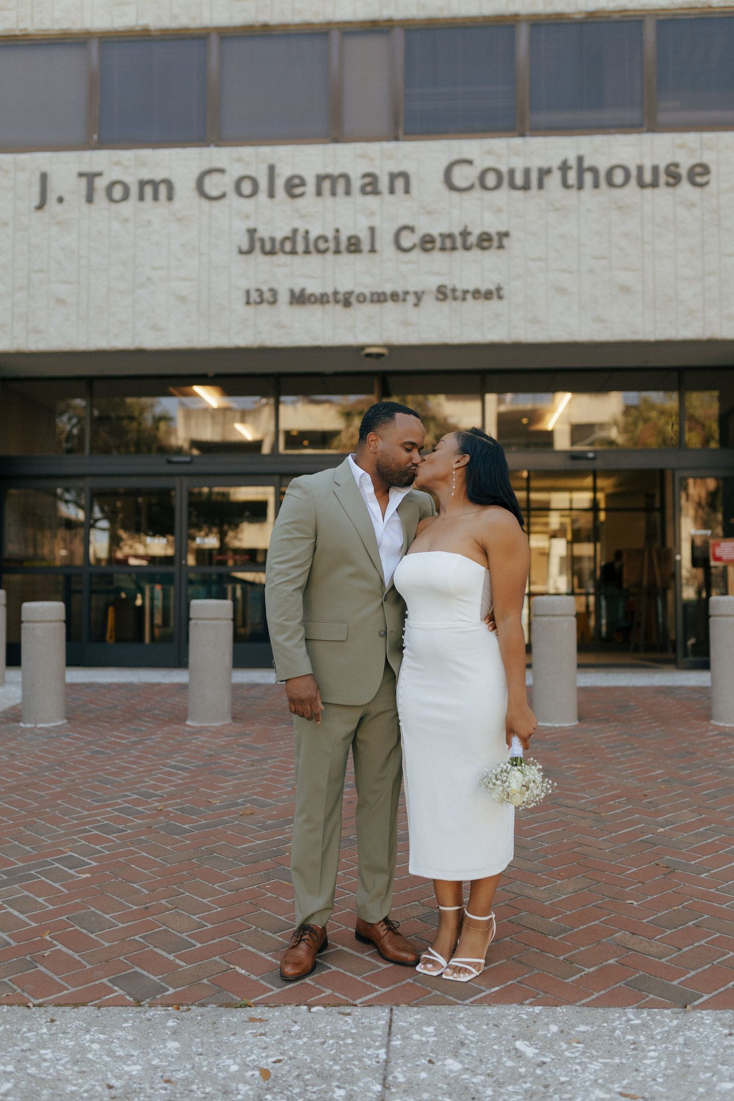A couple shares a romantic moment outside the J. Tom Coleman Courthouse wearing coordinated formal attire.