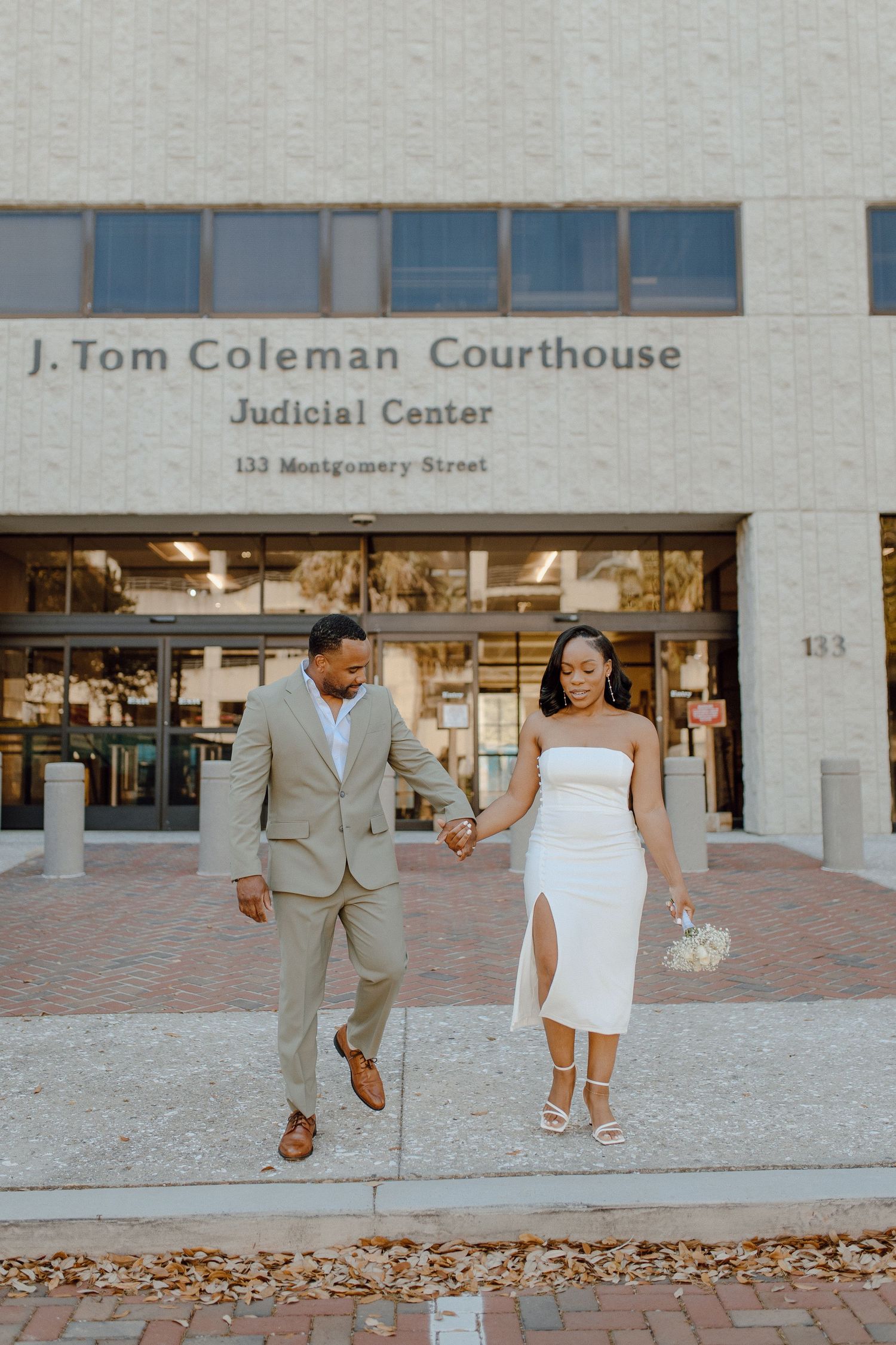 A couple celebrates their wedding day outside the J. Tom Coleman Courthouse, with the bride in white and groom in tan suit.