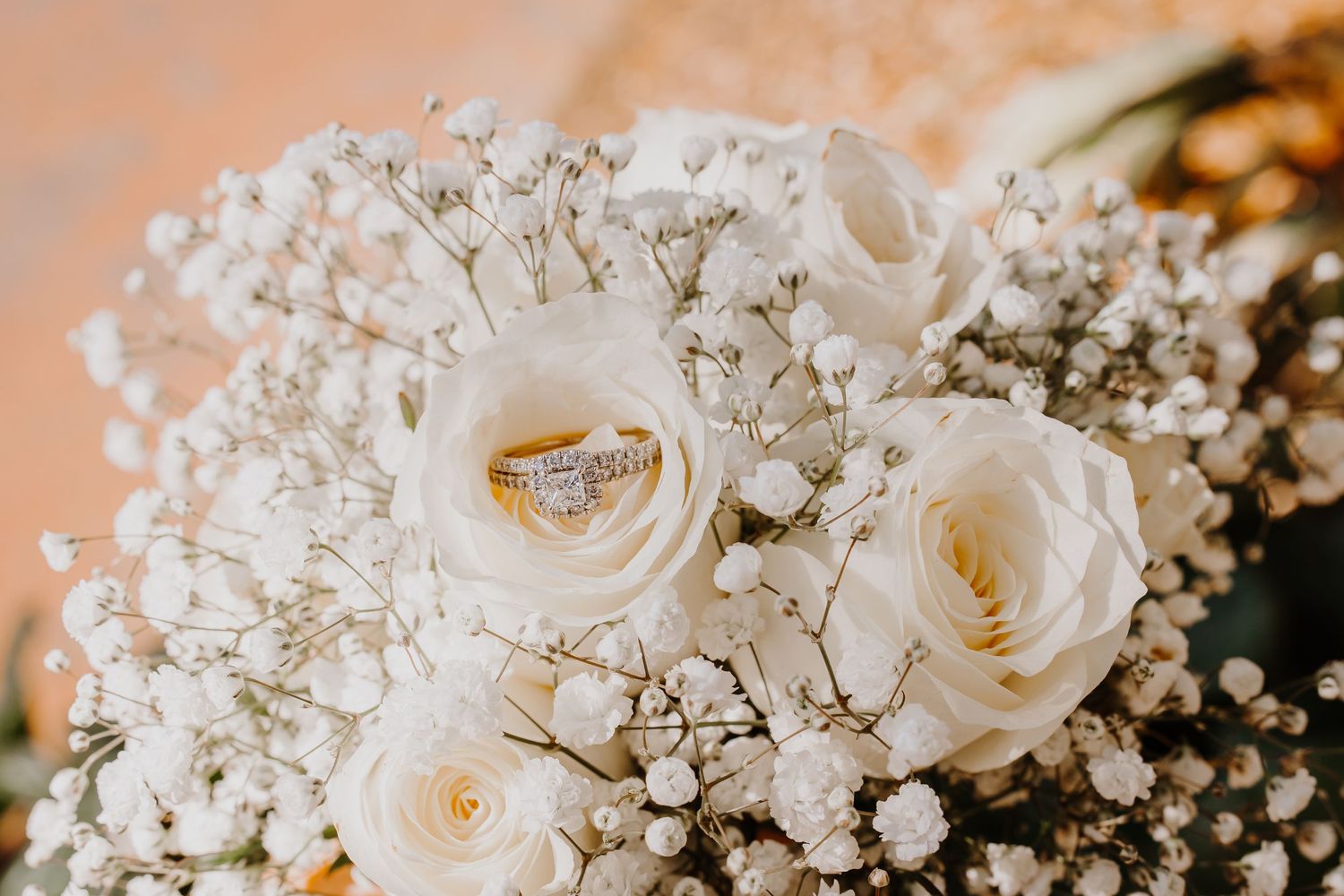 Wedding rings nestled between delicate white roses and baby's breath flowers in a romantic bridal bouquet.