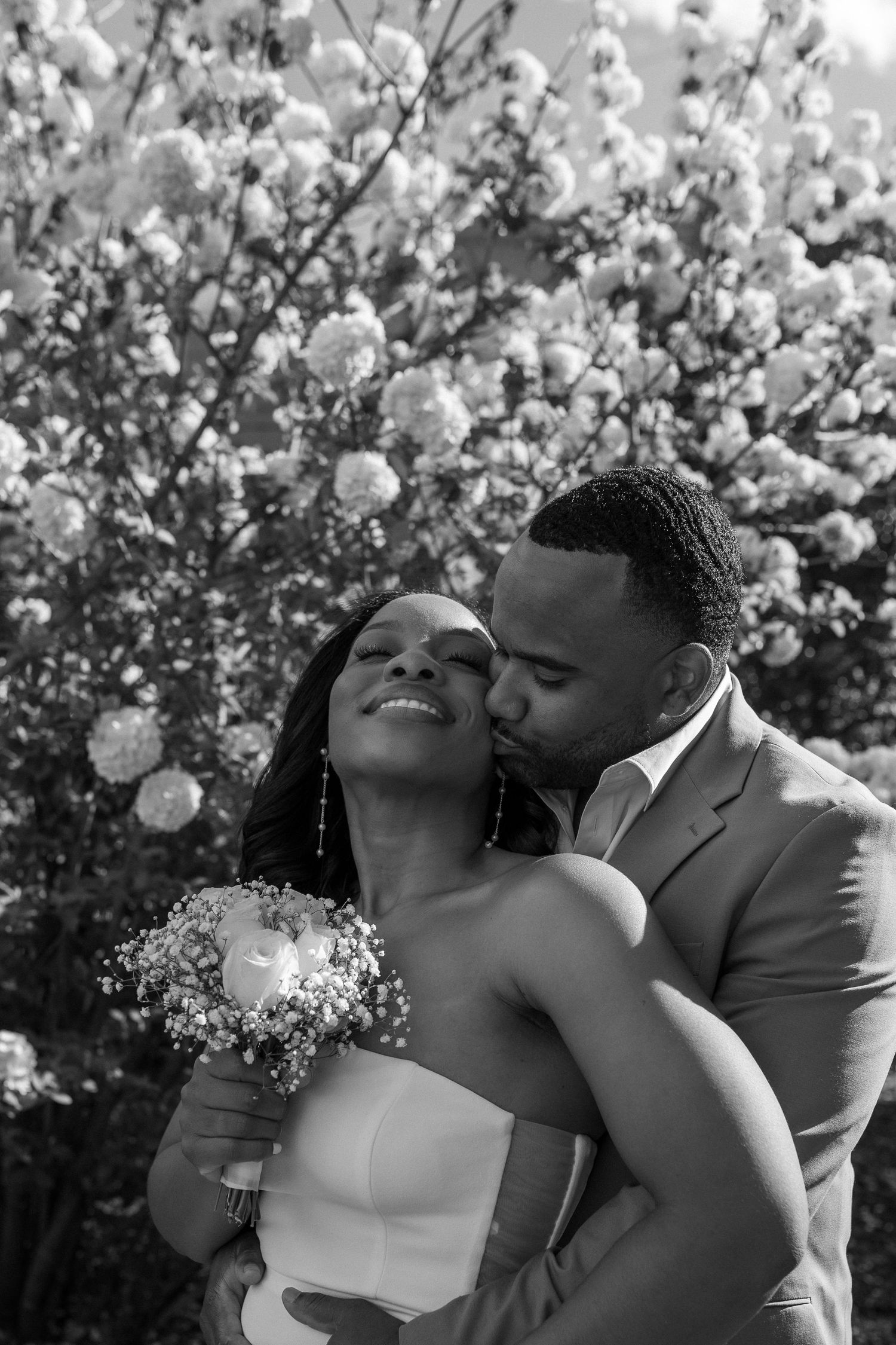 Black and white portrait of an intimate moment between a newly married couple with cherry blossoms in background.