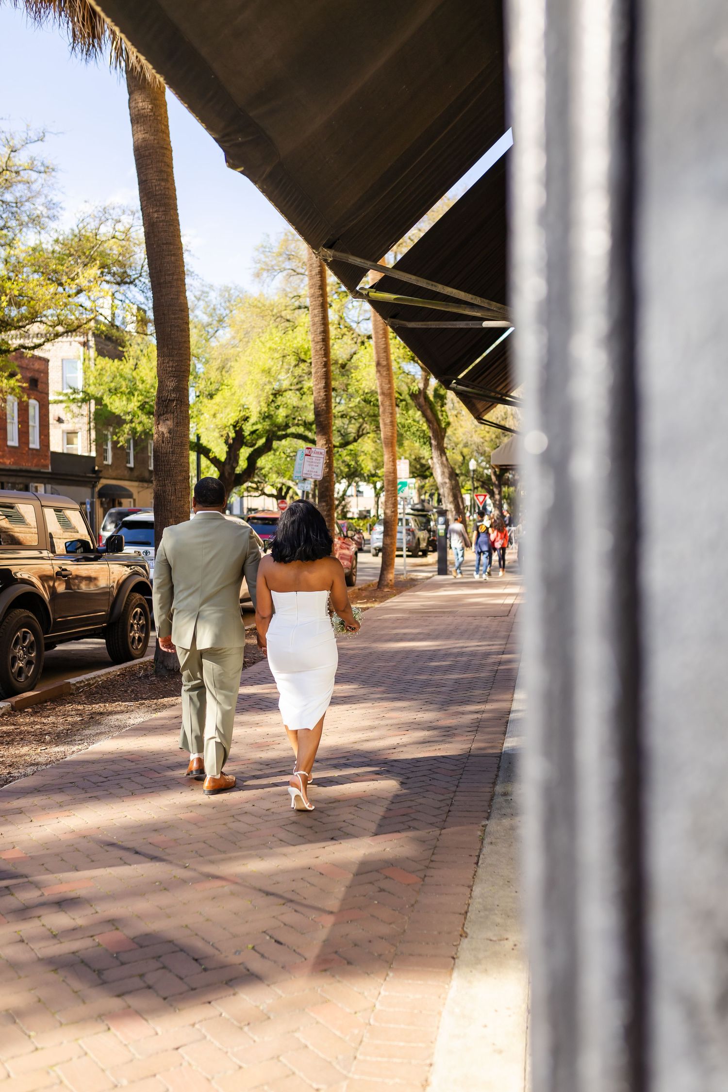 Couple walking hand in hand on a brick sidewalk under an awning in a charming downtown setting on a sunny day.