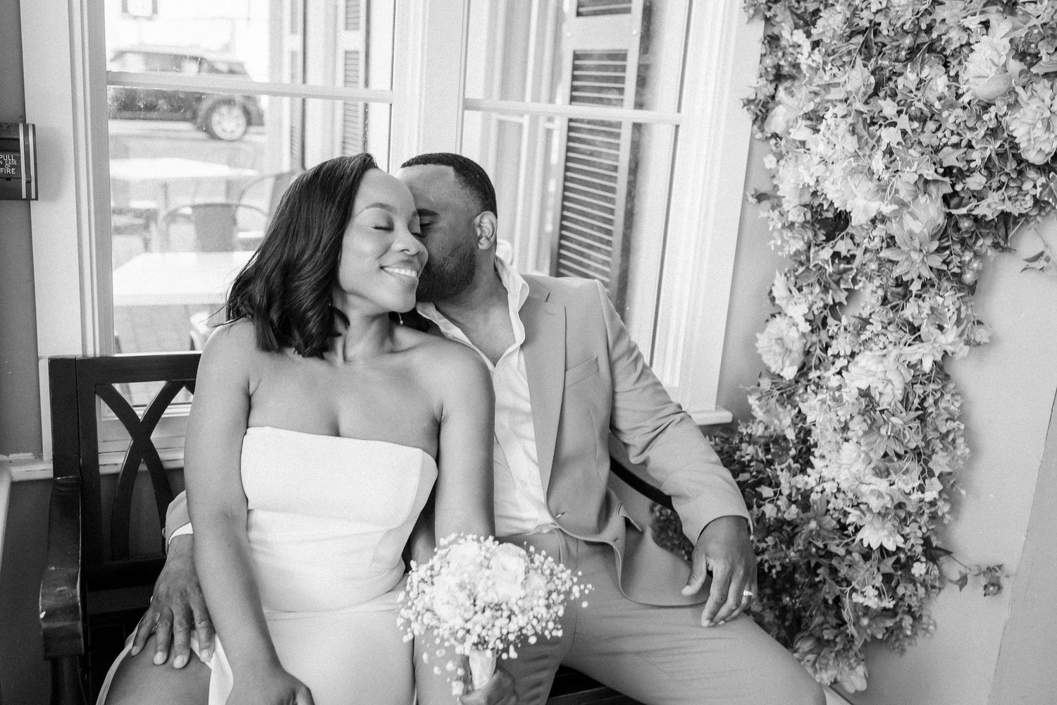 A tender black and white romantic moment between a couple sitting together at a floral-decorated venue.