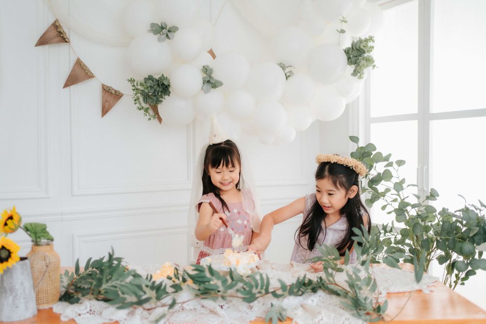 Bright celebration setup with white balloons, greenery and sunflowers against a white wall.