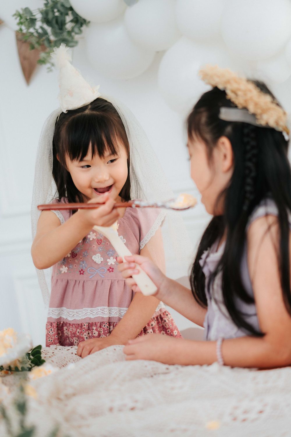 Two people in pink dresses share a playful moment during a celebration.