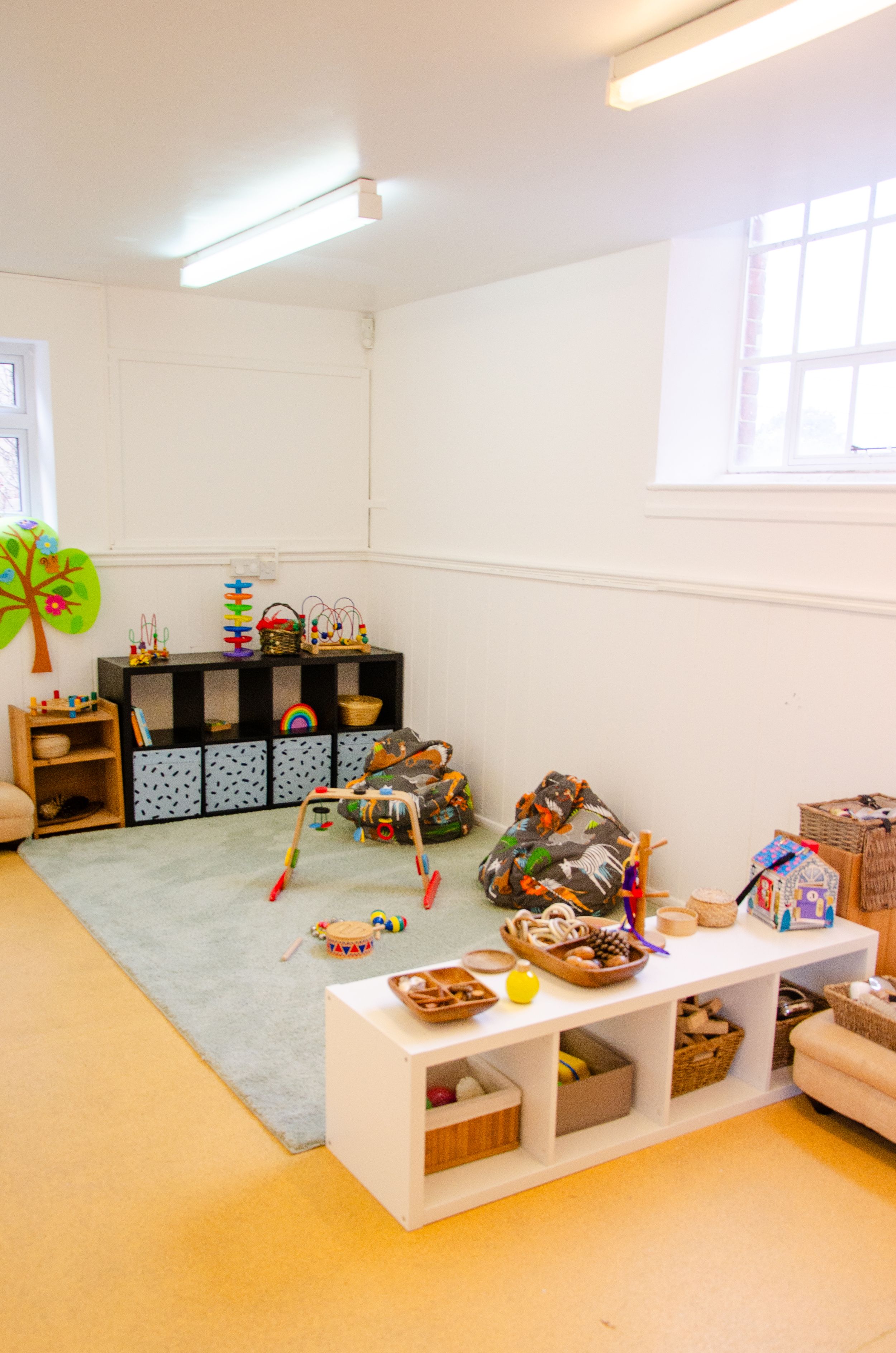 Bright playroom with storage cubes, toys, and a green rug on yellow flooring.