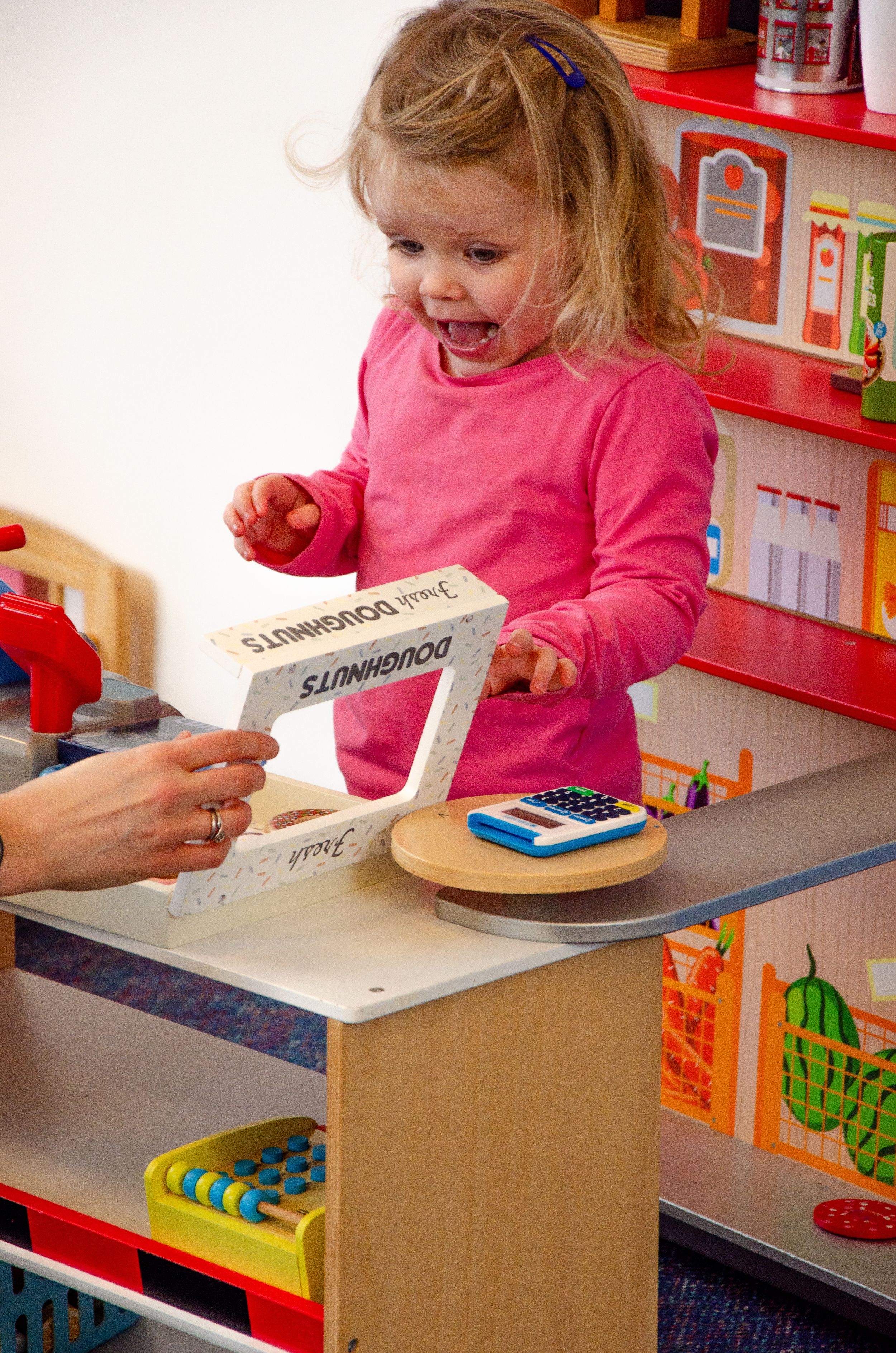 Play environment with toy cash register and shopping items on wooden counter.