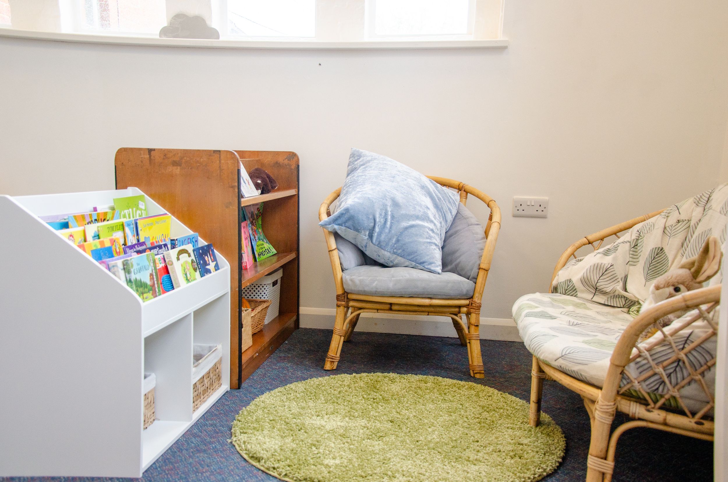 Cozy reading nook with rattan chairs, green rug, and children's book storage.