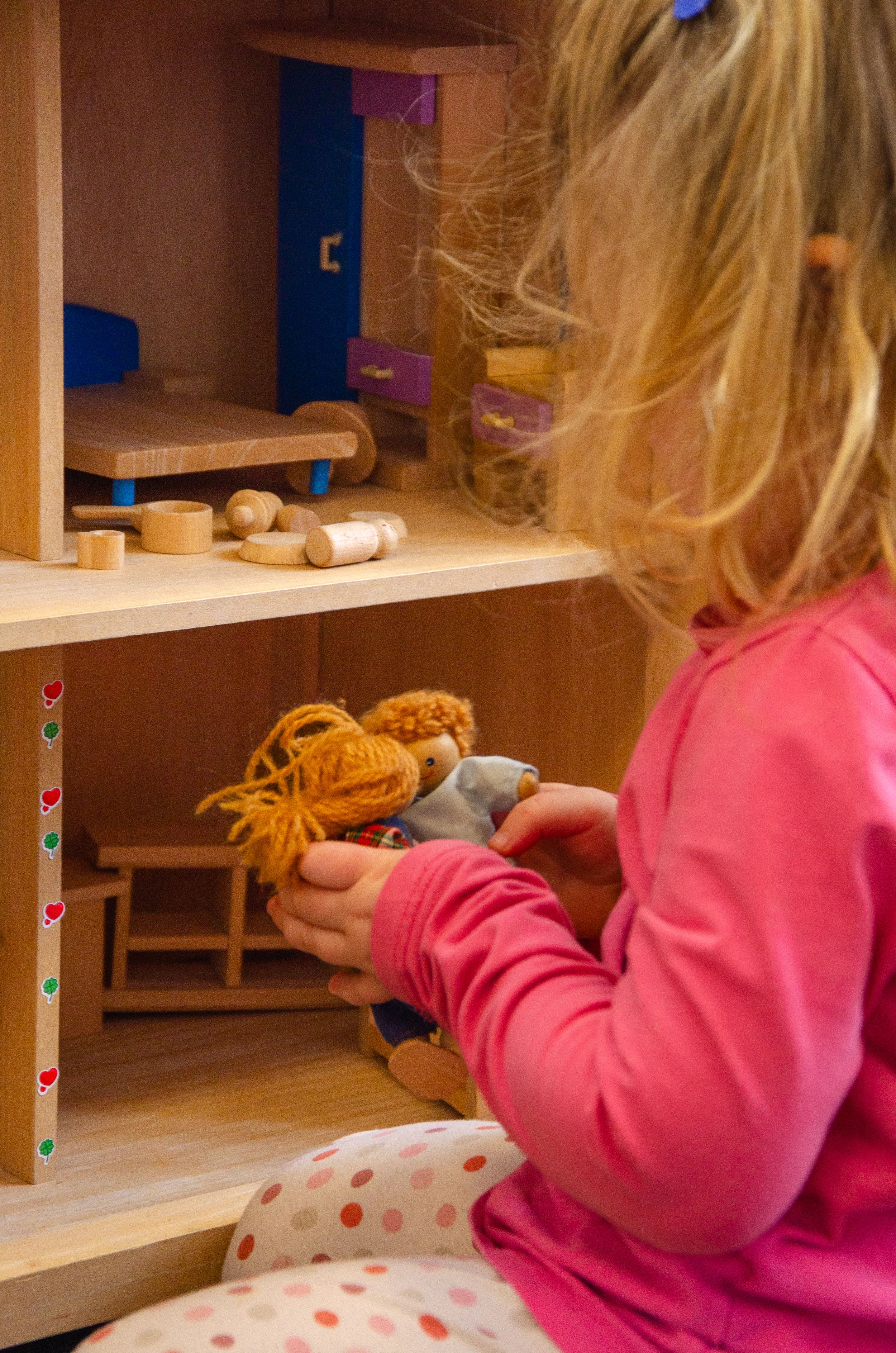 Wooden dollhouse with miniature furniture being played with.