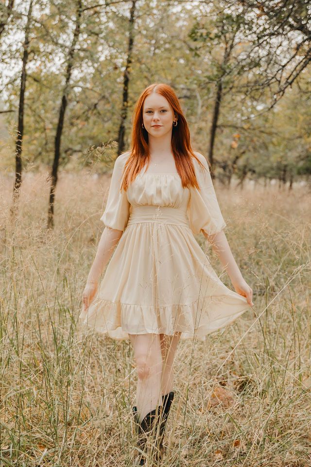 A dreamy outdoor portrait in a cream-colored dress among tall grasses and autumn trees.
