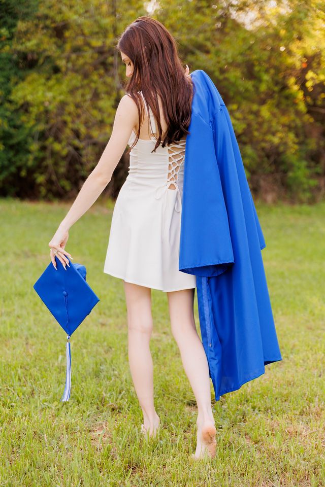 Graduation photo showing white dress and blue graduation gown in a grassy field.
