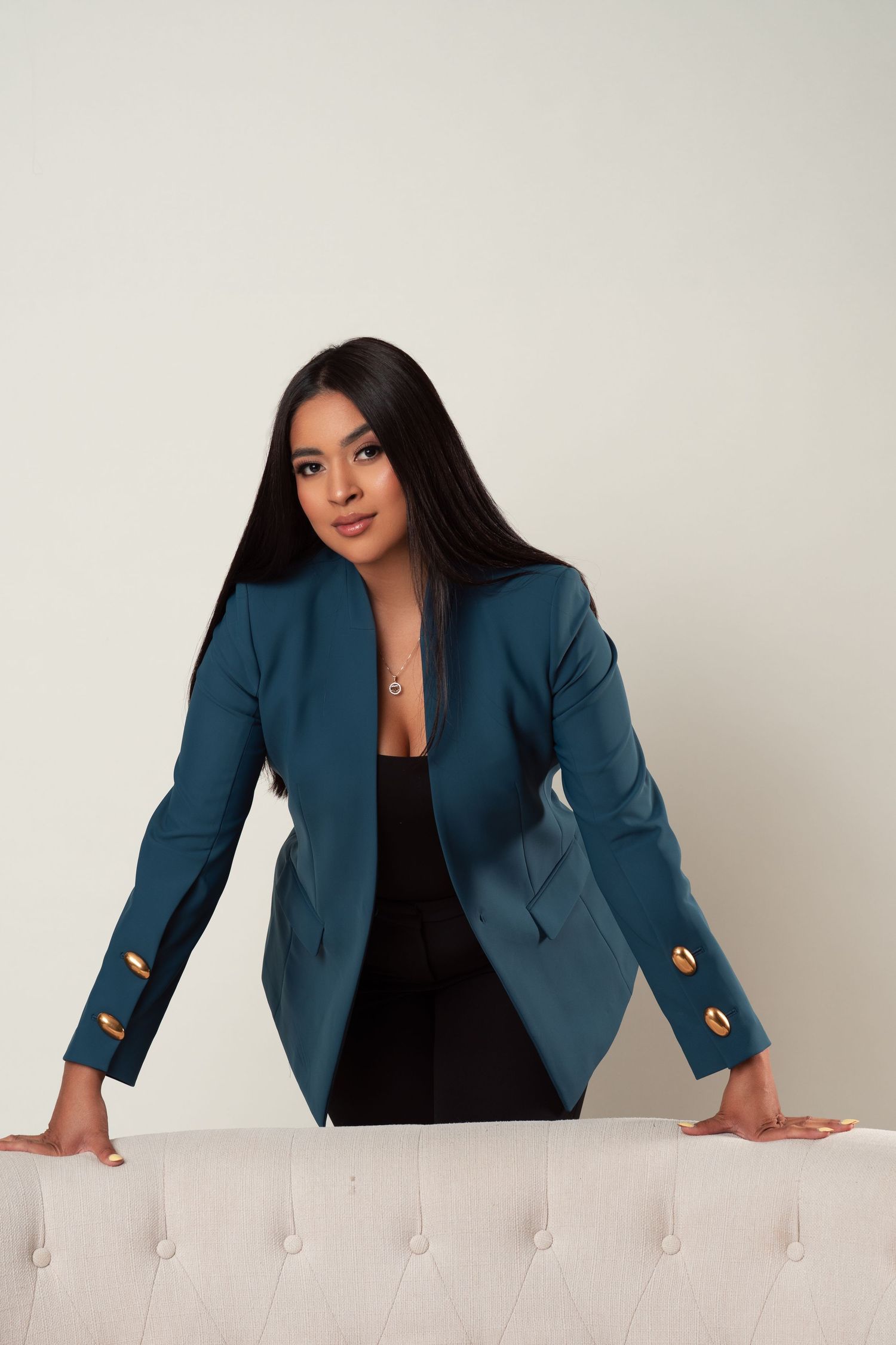 A woman poses against a dark background wearing a vibrant hot pink blazer over white pants.