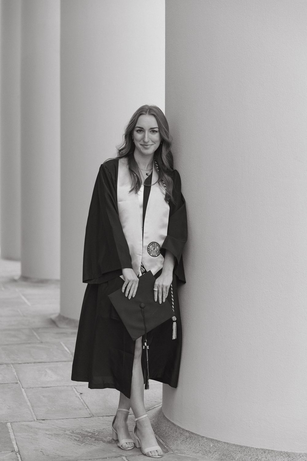 Black and white portrait of graduate in academic regalia between columns.