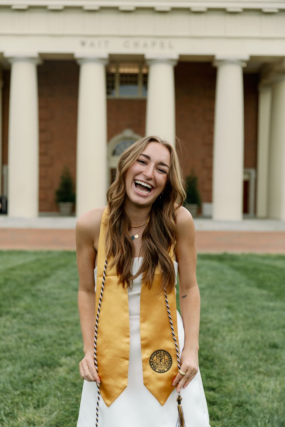Graduate celebrates on lawn in front of Wait Chapel wearing gold honors stole.