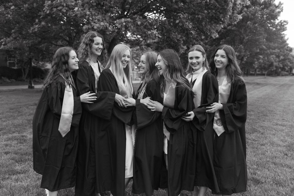 Group of graduates share joyful moment in black and white photo on campus grounds.