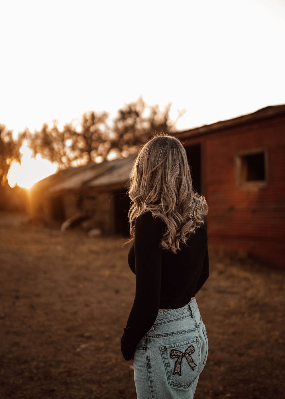 Back view of someone wearing a black top and light denim jeans against a sunset backdrop.