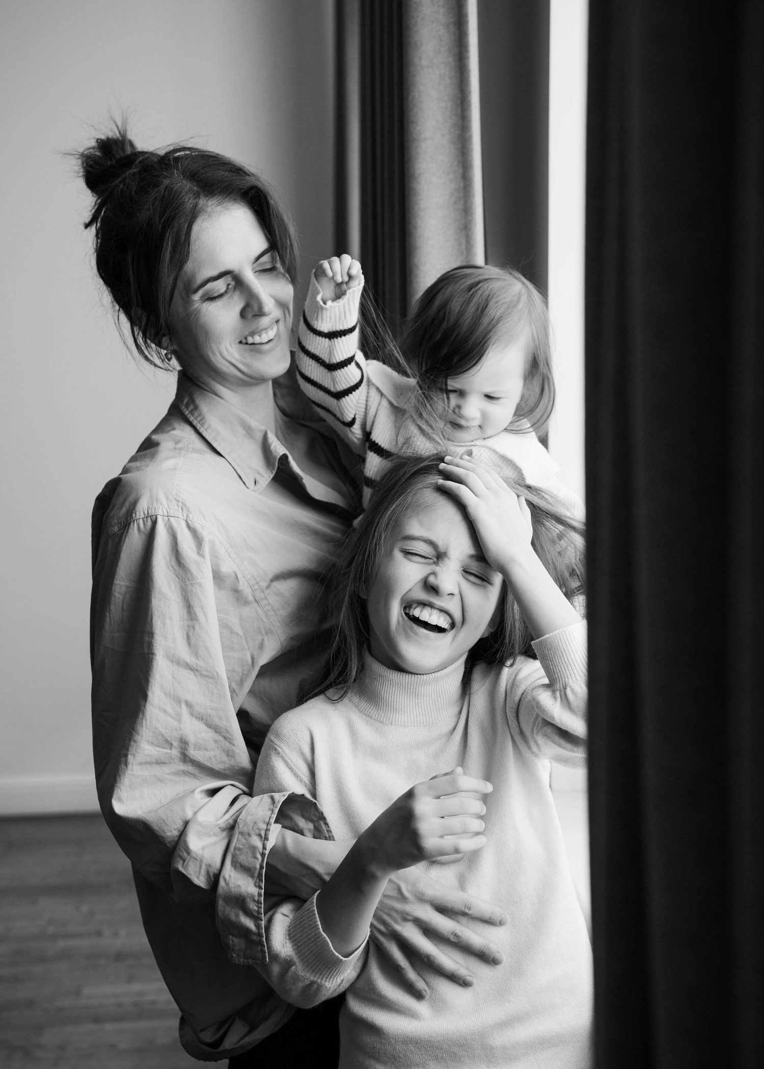 A mother and two daughters are standing together and laughing.