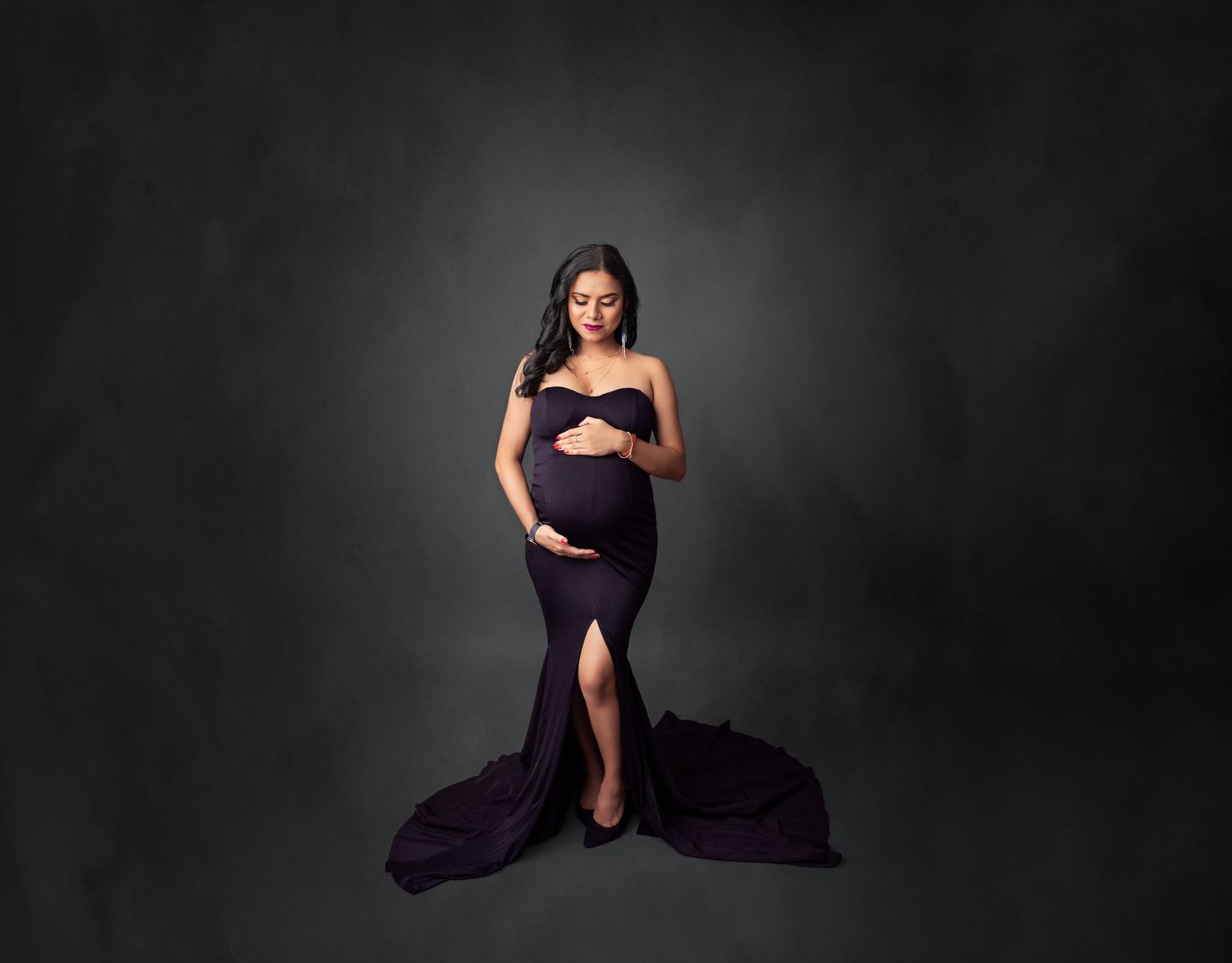 Dramatic maternity photo with purple gown against dark backdrop.
