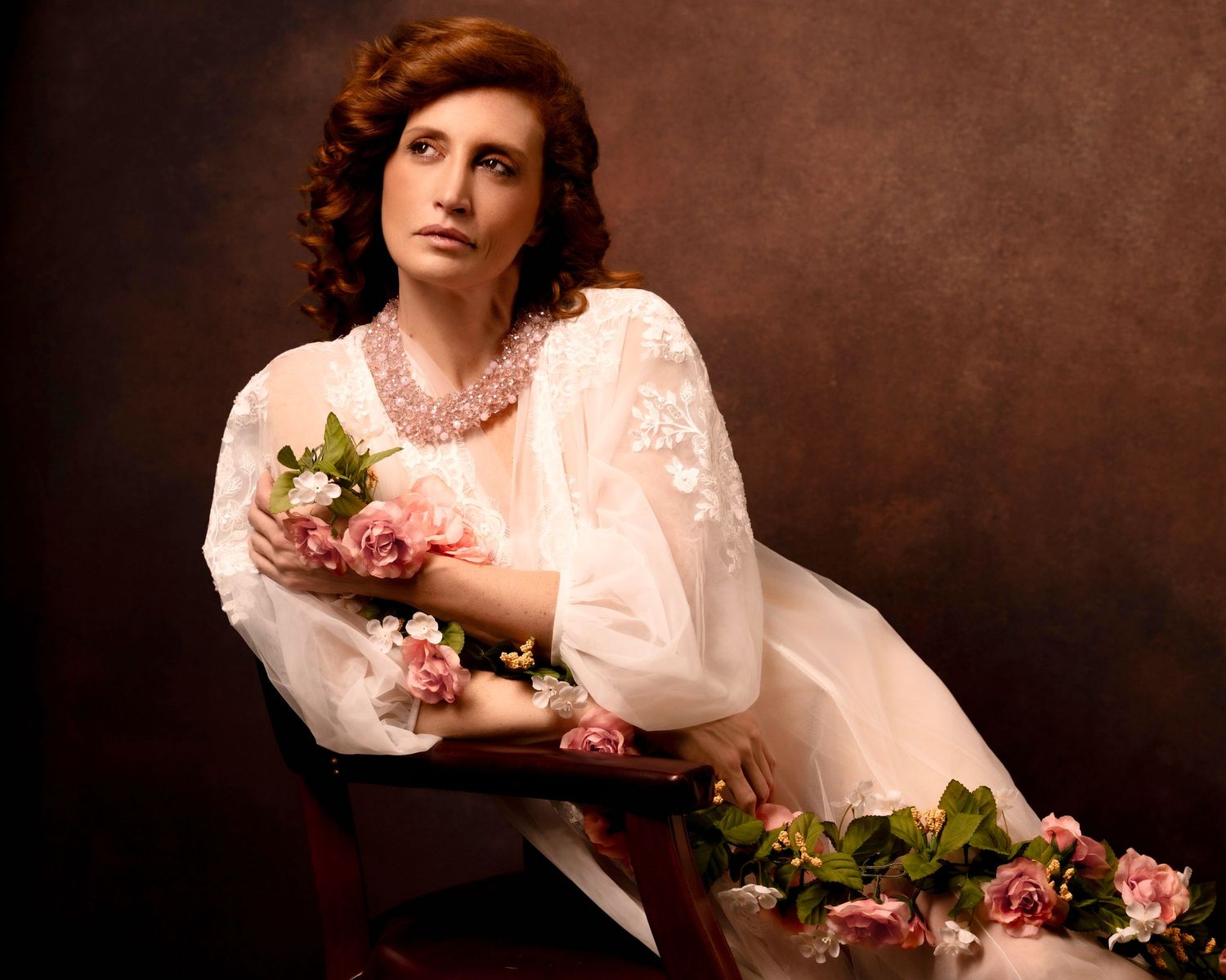Artistic portrait with roses in vintage-inspired white lace dress against brown background.