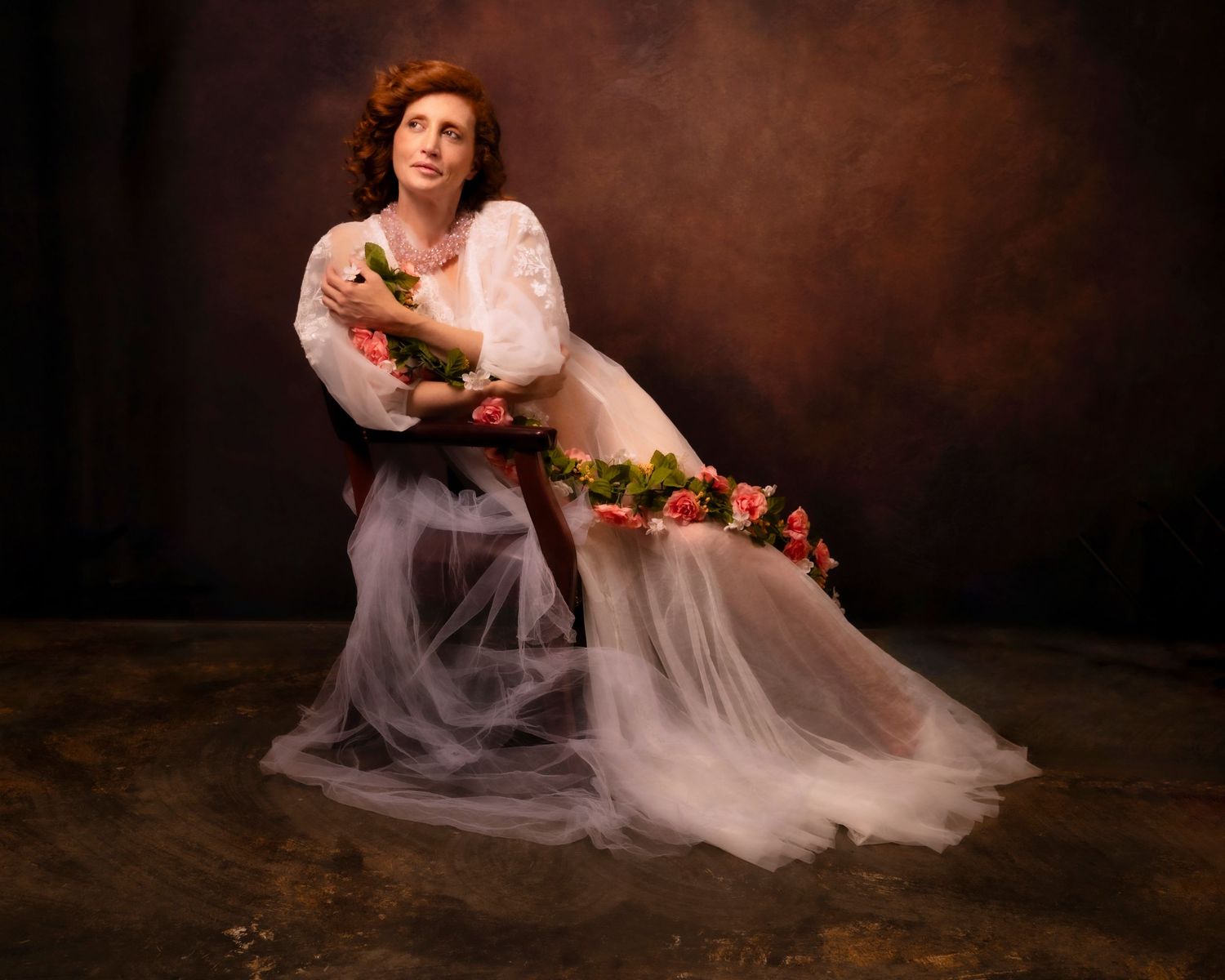 Romantic portrait in flowing white dress with floral garland against dark backdrop.