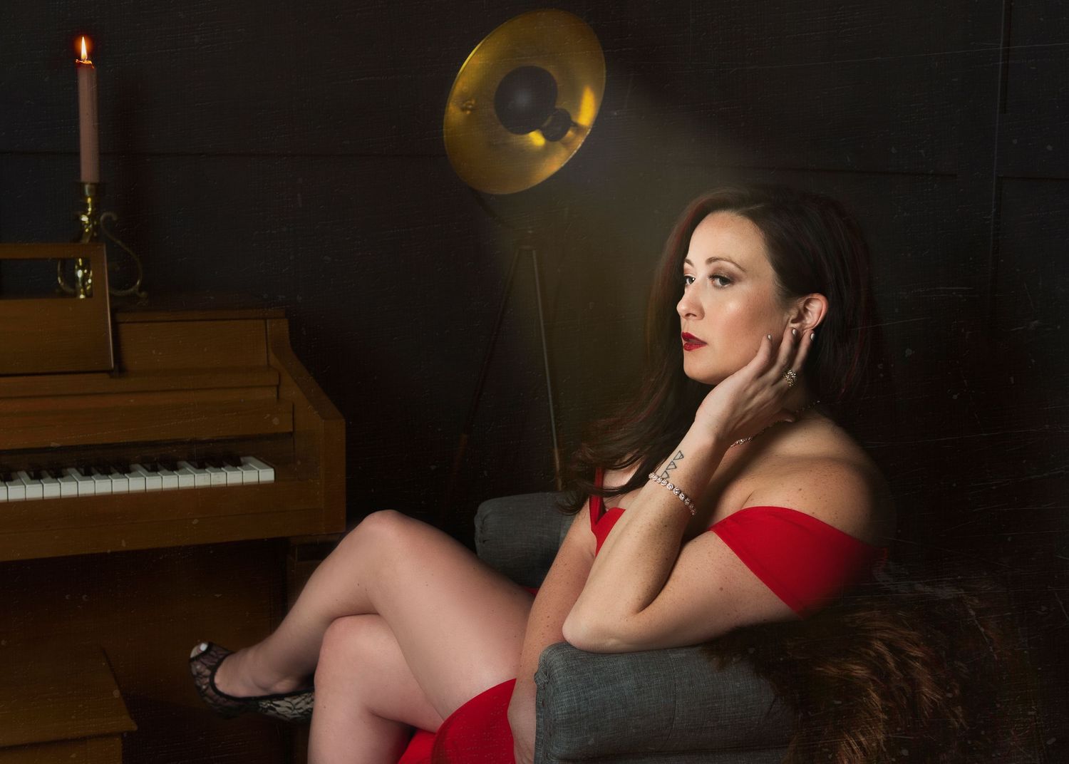 Vintage-style boudoir portrait with piano and brass lamp in dark setting.