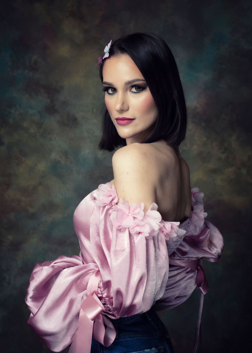 Elegant portrait in pink off-shoulder top with dramatic lighting and textured background.