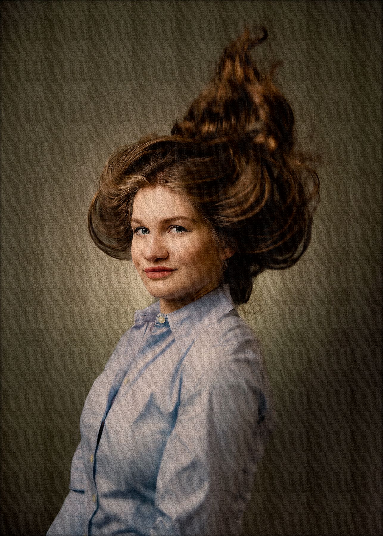 Creative portrait with dynamic hair motion in a light blue button-up shirt against neutral background.