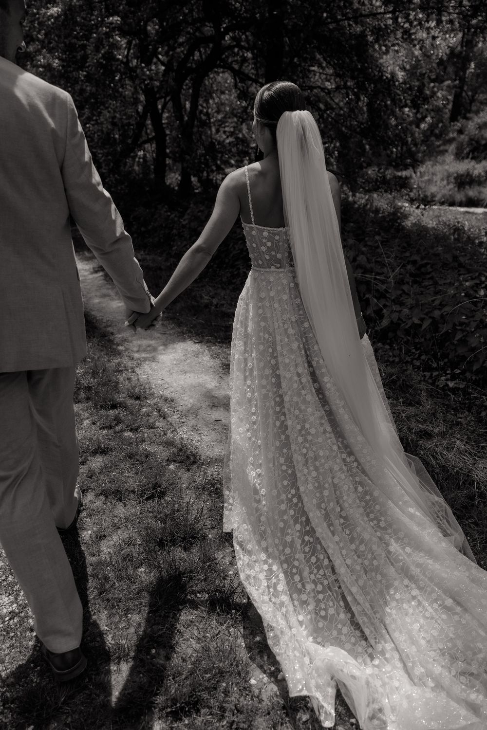 A black and white portrait of a wedding dress train flowing on a garden path.
