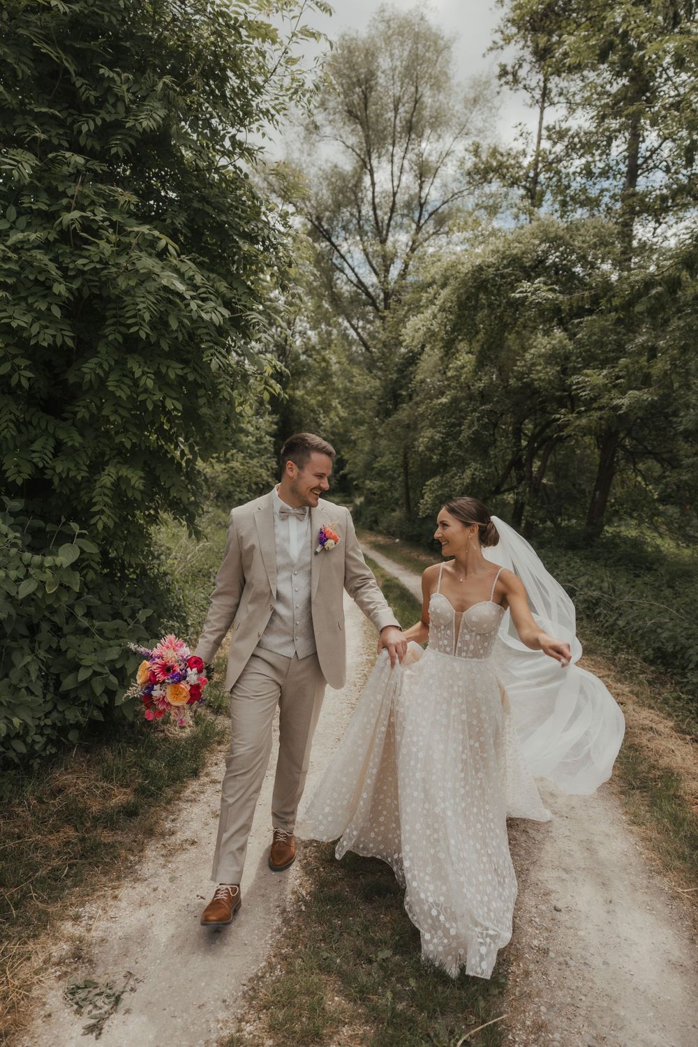 A couple shares joyful moments walking along a sunlit forest path.