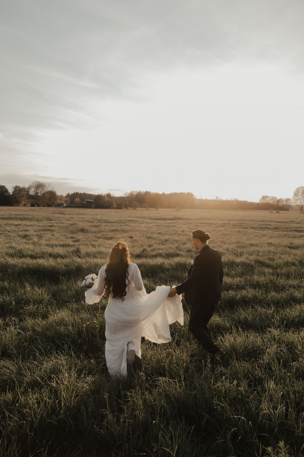Couple dancing together in a golden sunlit meadow with flowing white dress and dark suit.