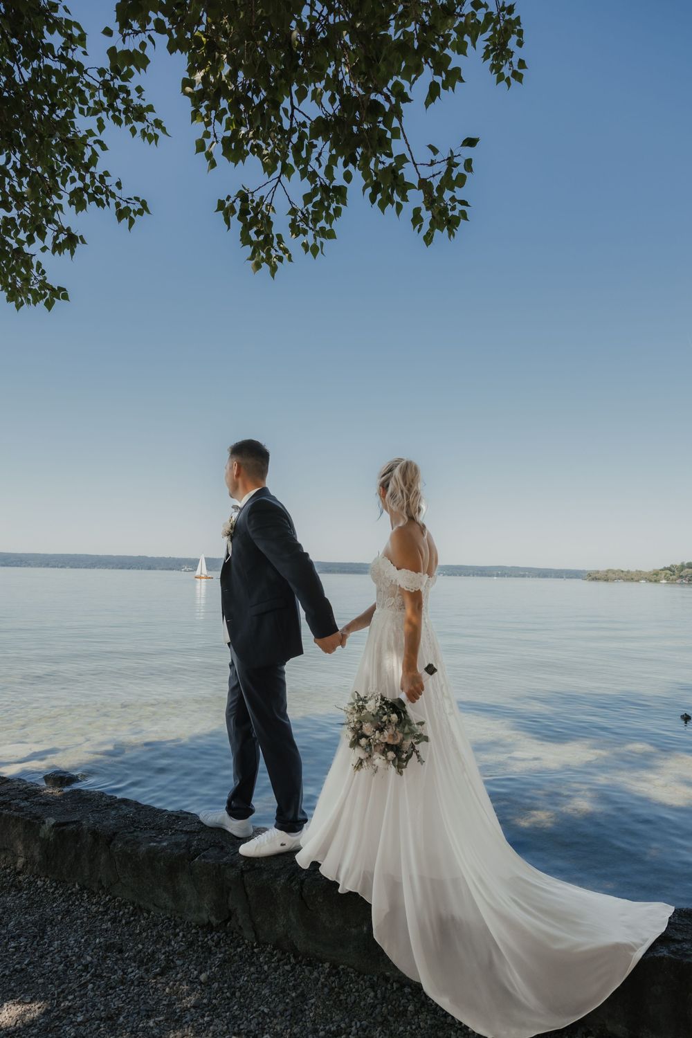 Couple standing at waters edge with flowing wedding dress caught in the breeze.
