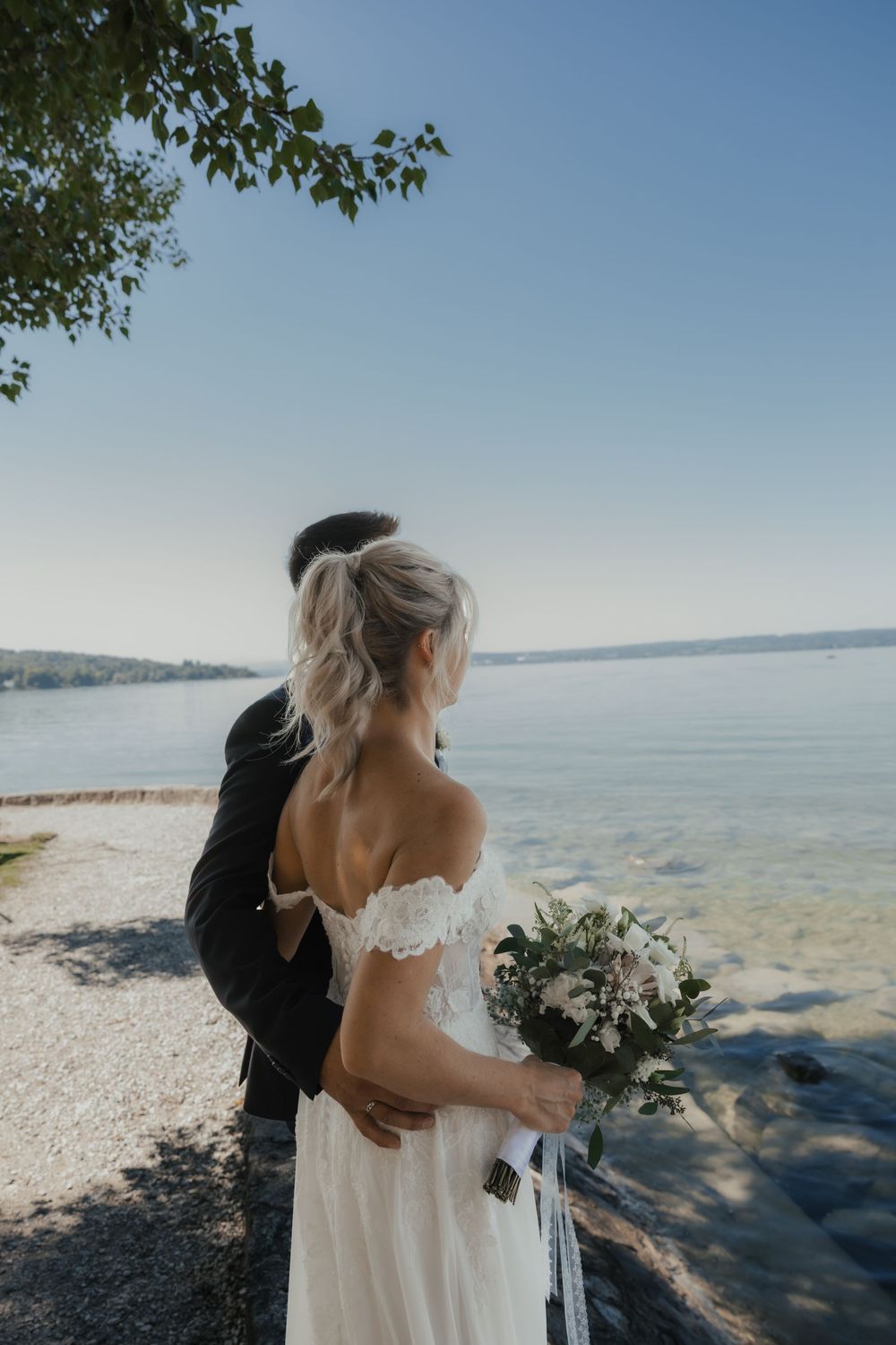 Wedding couple embracing near the water's edge on a sunny coastline.