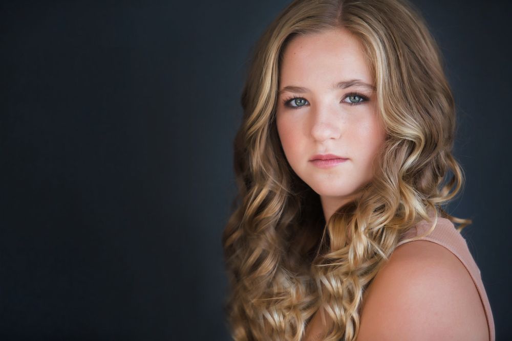 Professional headshot of a woman with long wavy blonde hair against a dark backdrop.