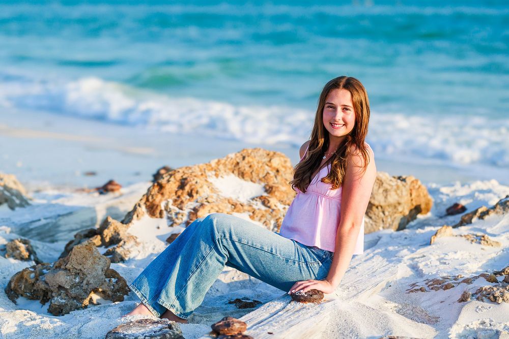 Woman in denim lying on beach sand with turquoise ocean waves in background during sunset photoshoot.