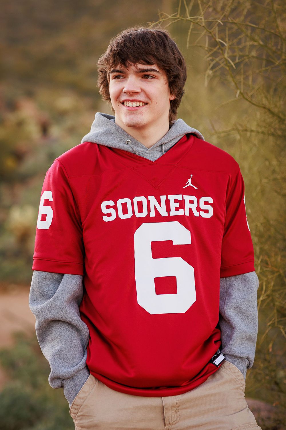 Person wearing a red Sooners #6 jersey with grey hoodie outdoors.