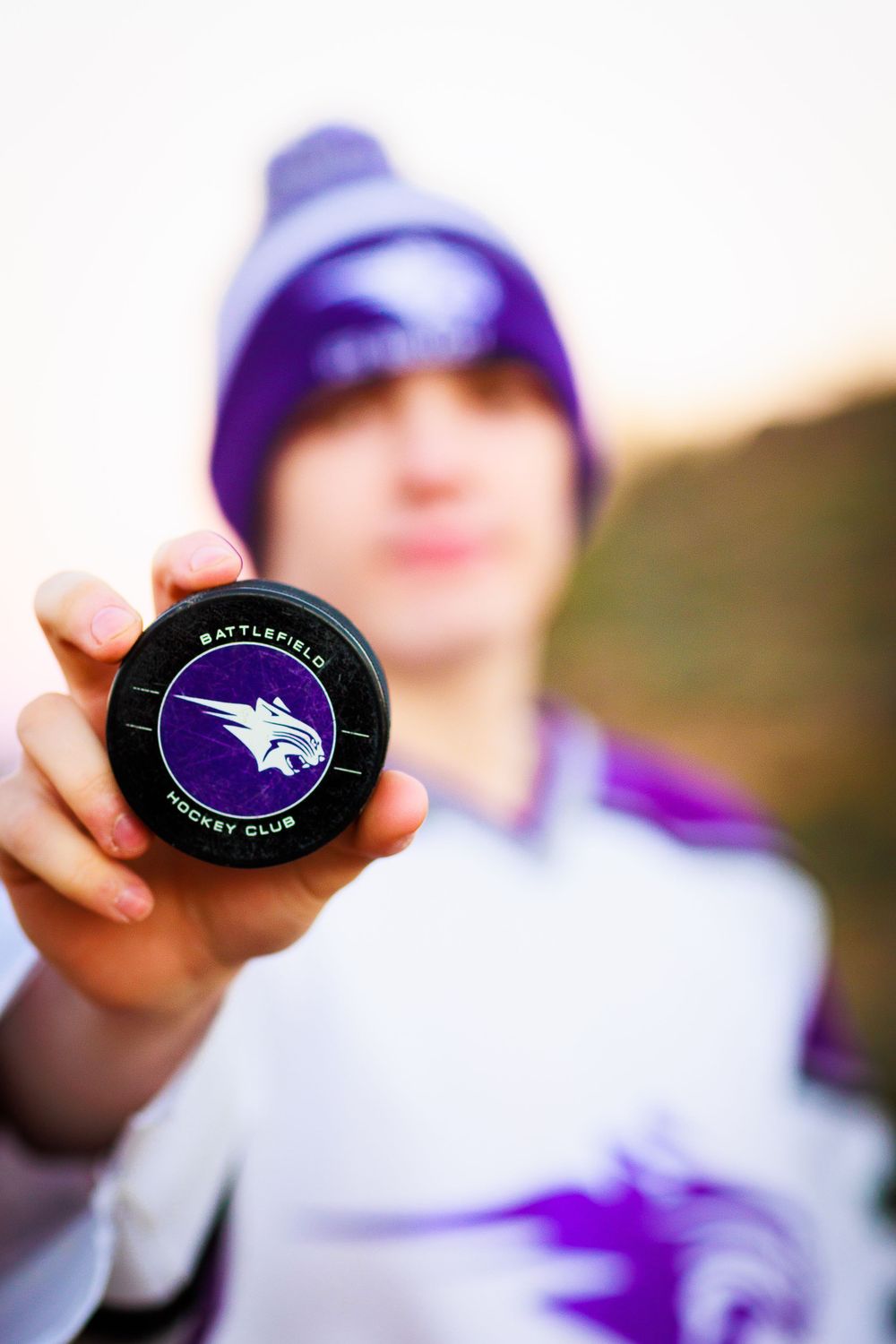 Close-up of a hand holding a purple sports puck with a wolf logo.