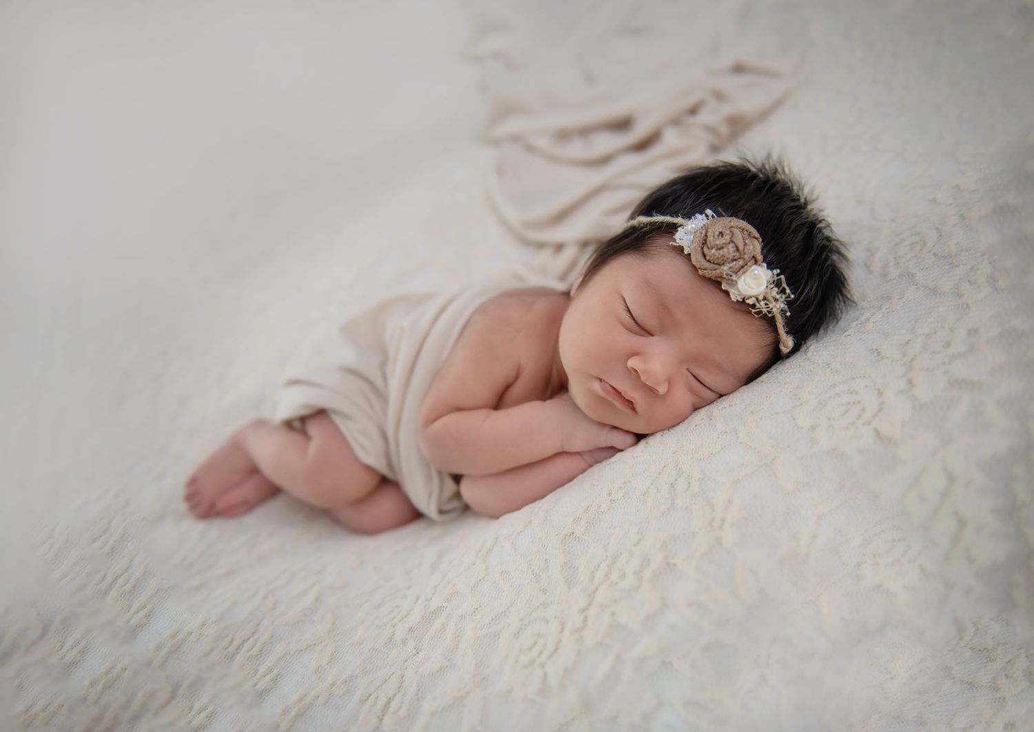 A sleeping newborn wearing a delicate headband on white fluffy fabric.