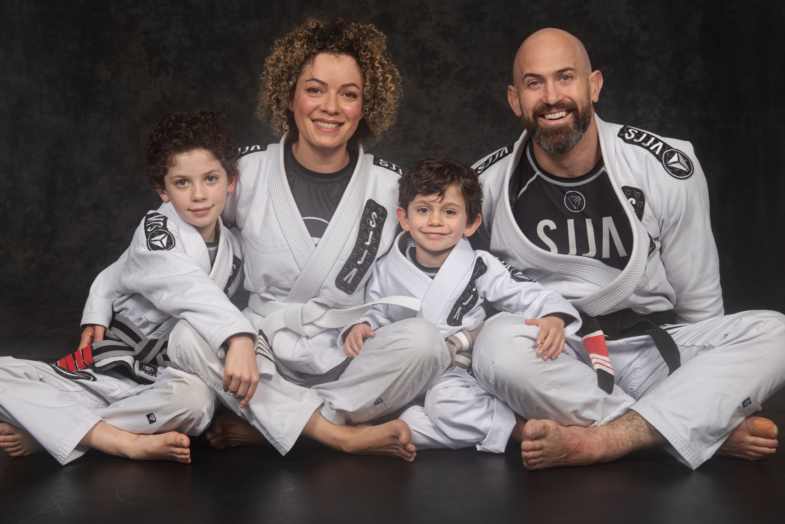 A family wearing white martial arts uniforms poses together against a dark background.