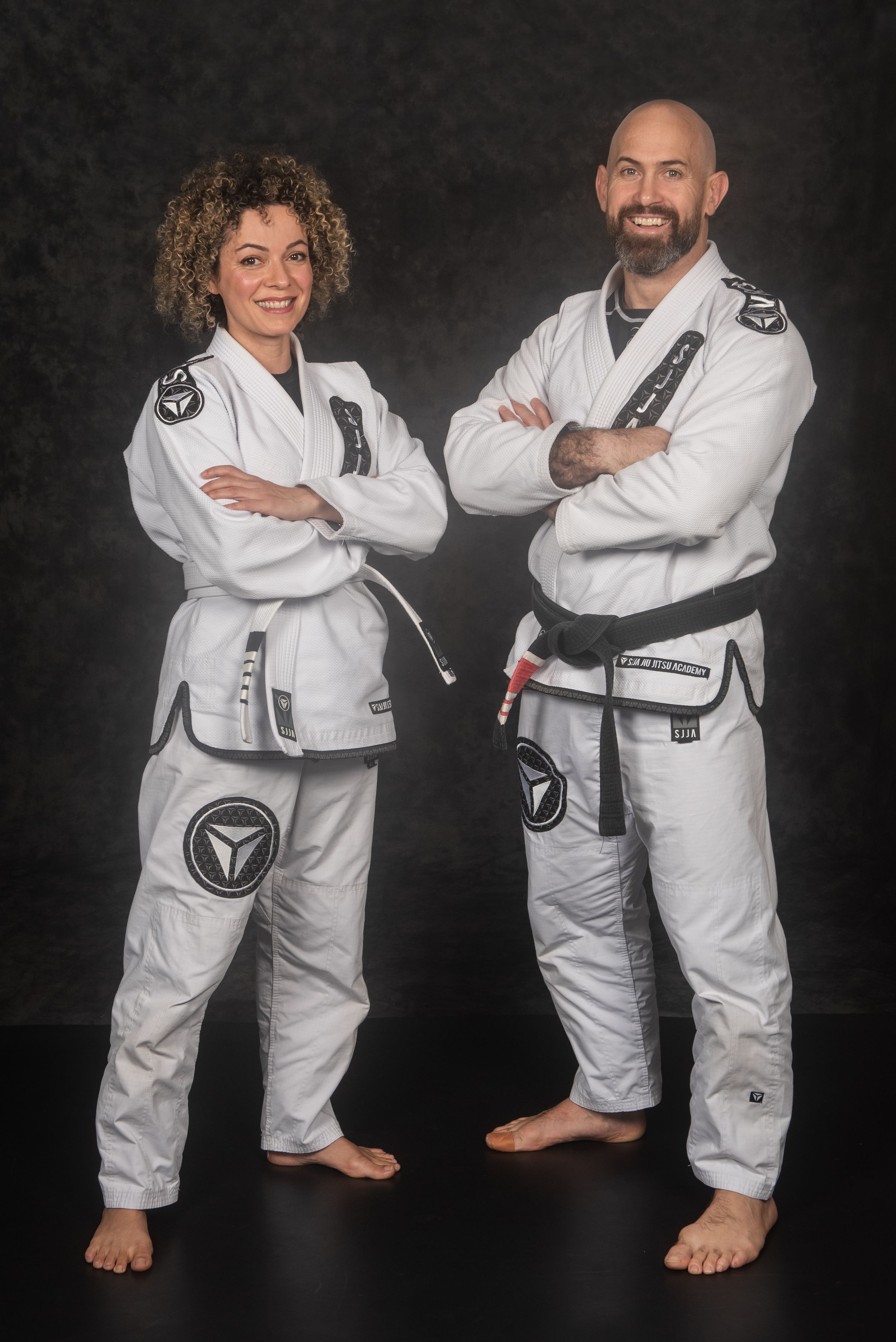 Two practitioners in white martial arts gis posing together against black backdrop.