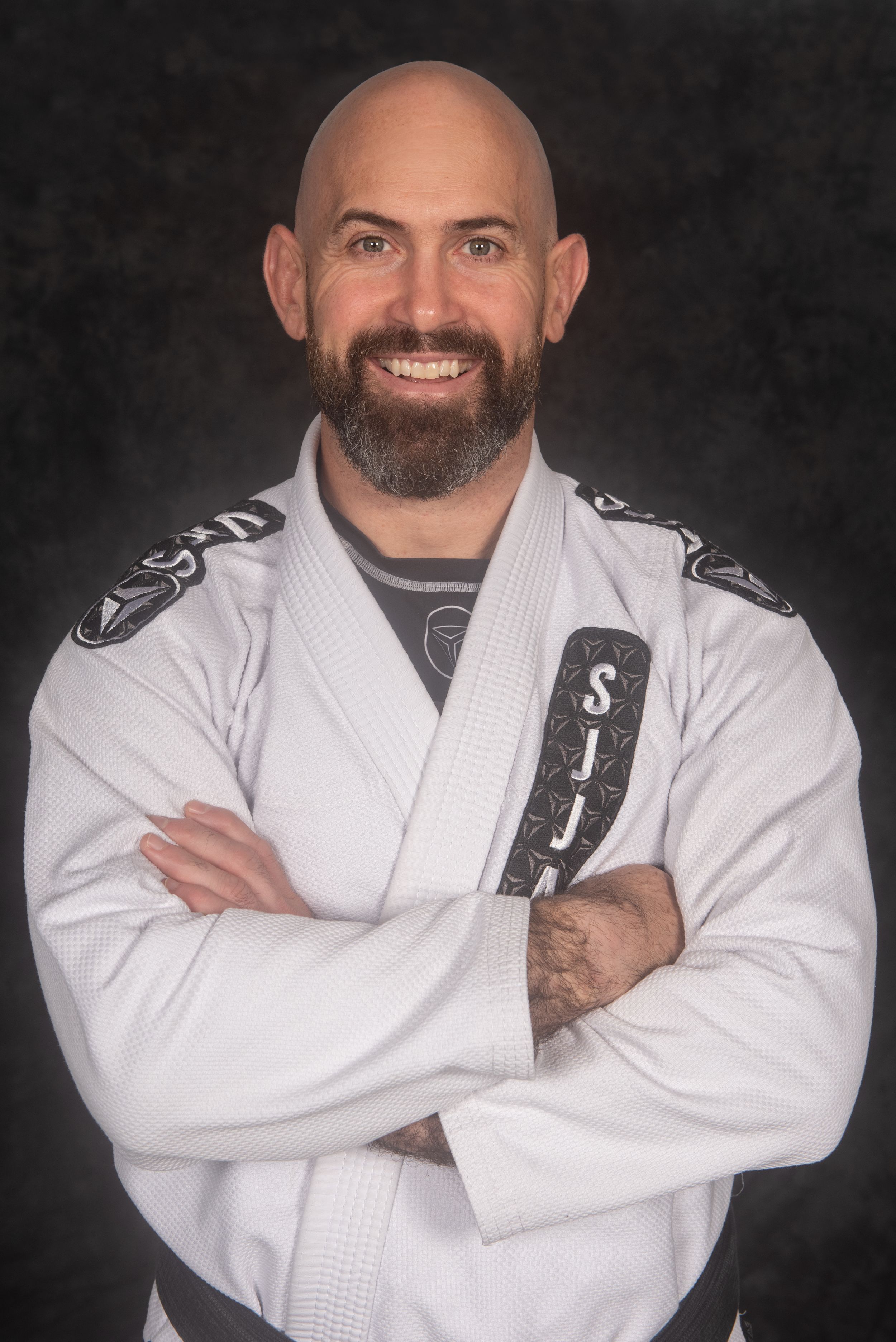 Martial artist with beard in white gi posing against dark studio background.